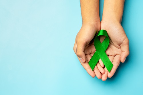 World Mental Health Day; green ribbon put in human's hands on bl