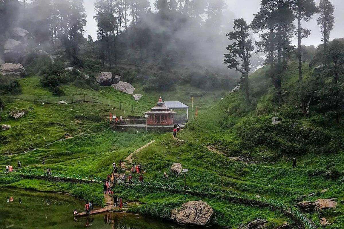Camping tents pitched in a green meadow surrounded by pine forest and snow-capped peaks in Tirthan Valley, Himachal Pradesh