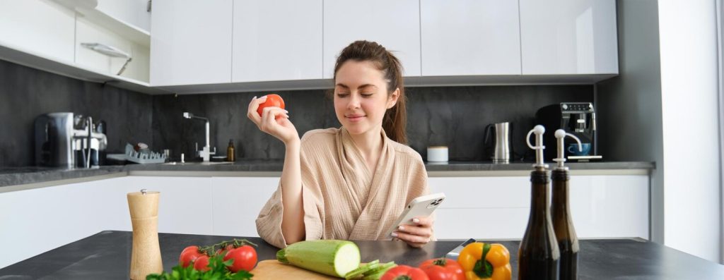 young-woman-orders-groceries-mobile-app-girl-bathrobe-sits-kitchen-with-vegetables_1258-198242